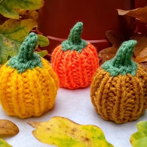 Puede incluir: Tres calabazas de punto en naranja, amarillo y marrón. Las calabazas son todas del mismo tamaño y tienen un tallo verde.