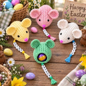 May include: Four knitted mouse-shaped ornaments in pink, yellow, green, and white, each featuring black bead eyes, a pink nose, and a dangling string of letter beads spelling names like Daisy, Lily, Arthur, and April, with a chocolate egg inside.