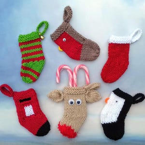 Puede incluir: Seis calcetines de Navidad tejidos con diferentes diseños. Los calcetines son rojos, verdes, marrones, blancos y negros. Un calcetín tiene un bastón de caramelo que sobresale.