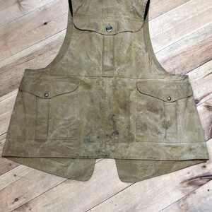 Pu&ograve; includere: Un gilet color cachi con pi&ugrave; tasche e chiusura con bottoni. Il gilet ha un aspetto vissuto, che suggerisce che sia realizzato in un materiale resistente. Presenta due ampie tasche sul davanti e una tasca pi&ugrave; piccola sul petto.