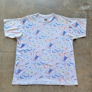 May include: White t-shirt with a repeating pattern of cartoonish figures, including eyes, skeletons, and the word "BOIN" in a stylized font. The design incorporates blue, red, yellow, and green elements.