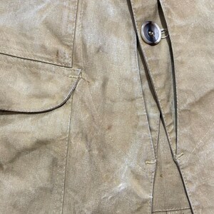 Pu&ograve; includere: Primo piano di una giacca beige con chiusura a bottoni e una tasca. La giacca ha un aspetto strutturato e dettagli di cucitura visibili. Il bottone &egrave; marrone chiaro.