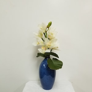 Faux white Cymbidium orchid stem, potted in a blue glazed ceramic bud vase with faux Galax  leaves.