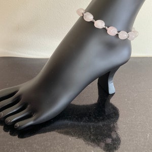 May include: A delicate anklet made with light pink, oval-shaped beads and silver accents.