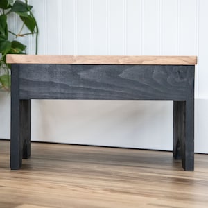May include: A small wooden stool with a black stained top and legs. The stool is made of wood and has a simple design.