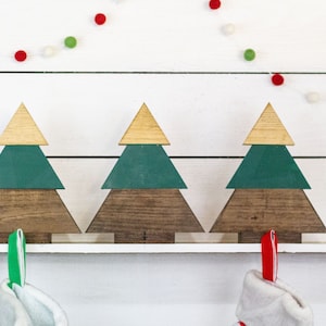 May include: Three wooden Christmas tree stocking holders with a green and brown paint finish. Each holder has a hook for hanging stockings.