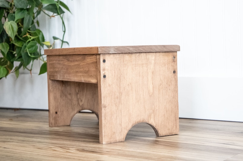 May include: A wooden step stool with a natural finish. The stool has a rectangular top and curved legs.