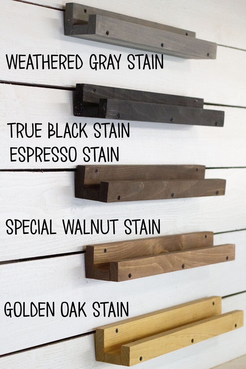 Op de afbeelding: Vijf houten planken in verschillende beitskleuren, gemonteerd aan een witte muur. De planken zijn gelabeld met hun beitskleuren: Weathered Gray Stain, True Black Stain, Espresso Stain, Special Walnut Stain en Golden Oak Stain.