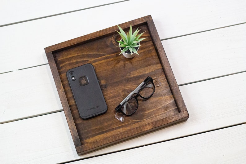 Op de afbeelding: Een houten dienblad met een zwarte telefoonhoes, een zwart brilletje en een klein plantje in een pot.