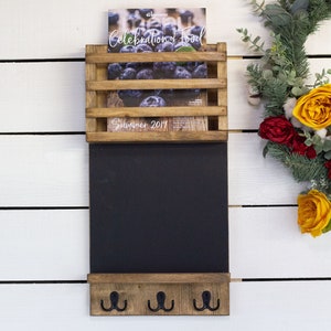 May include: Wooden wall organizer with a magazine rack, chalkboard, and three hooks. The magazine rack has a magazine with blueberries on the cover and the text "Celebration of Food Summer 2019".