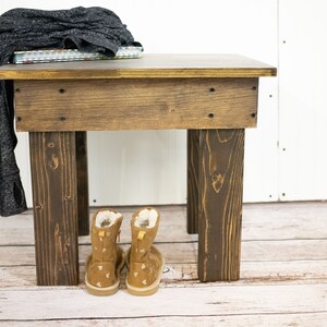 May include: A dark brown wooden end table with a square top and four legs. A gray sweater and a stack of books are on top of the table. Two brown suede boots with white accents are under the table. The text "ESPRESSO" is on the floor.