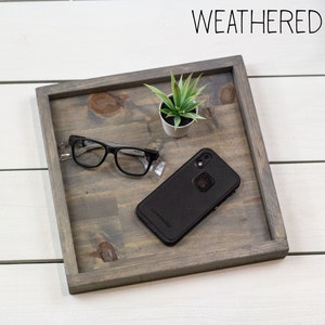 Op de afbeelding: Een verweerd grijs houten dienblad met een kleine plant in een pot, een bril en een zwarte smartphone in een beschermhoes.