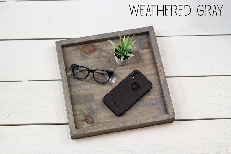 Op de afbeelding: Een verweerd grijs houten dienblad met een kleine plant in een pot, een bril en een zwarte smartphone in een beschermhoes.