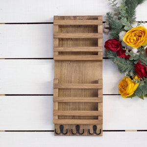 May include: A wooden wall mounted organizer with four shelves and five hooks. The organizer is stained a dark brown color. The organizer is mounted on a white wood plank wall.
