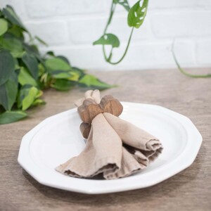 May include: A wooden napkin ring in the shape of a butterfly holds a beige linen napkin on a white plate.