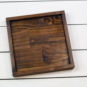 Op de afbeelding: Een vierkante houten dienblad van donkerbruin hout met een glad oppervlak. Het dienblad is gemaakt van hout en heeft een natuurlijke afwerking.