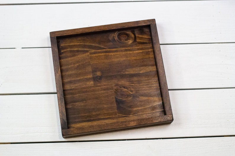 Op de afbeelding: Een vierkante houten dienblad van donkerbruin hout met een glad oppervlak. Het dienblad is gemaakt van hout en heeft een natuurlijke afwerking.
