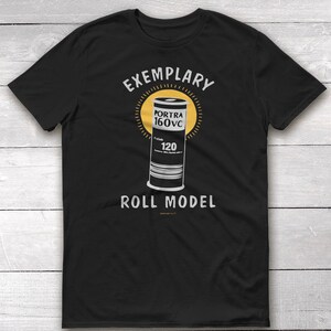 May include: Black t-shirt with a white graphic of a film canister with the text "EXEMPLARY" above and "ROLL MODEL" below. The canister has the text "PORTRA 160VC" and "120" on it.