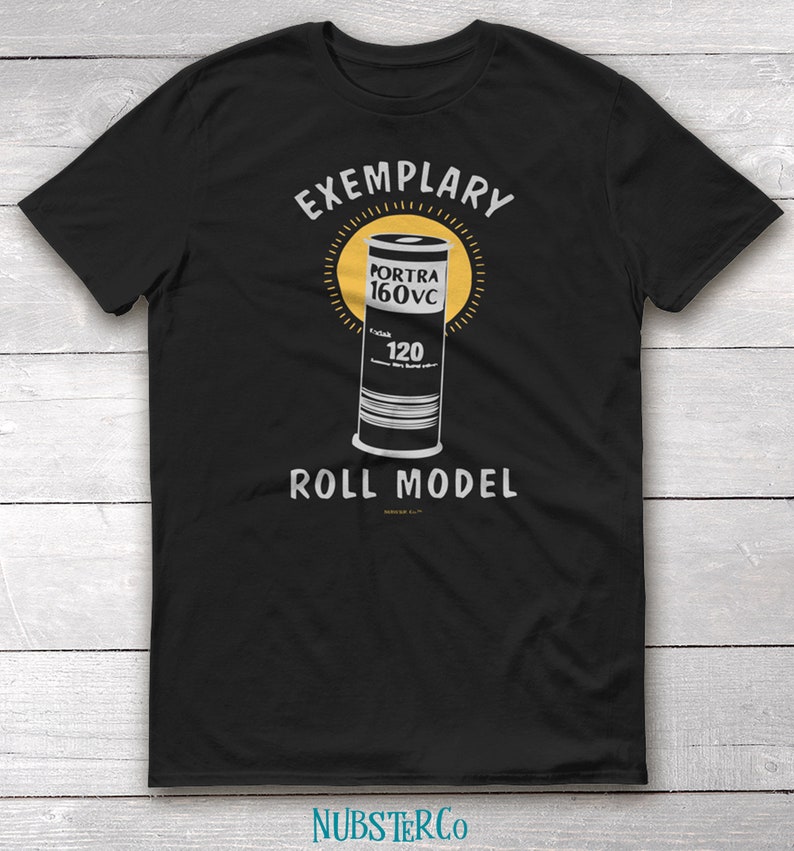 May include: Black t-shirt with a white graphic of a film canister with the text "EXEMPLARY" above and "ROLL MODEL" below. The canister has the text "PORTRA 160VC" and "120" on it.