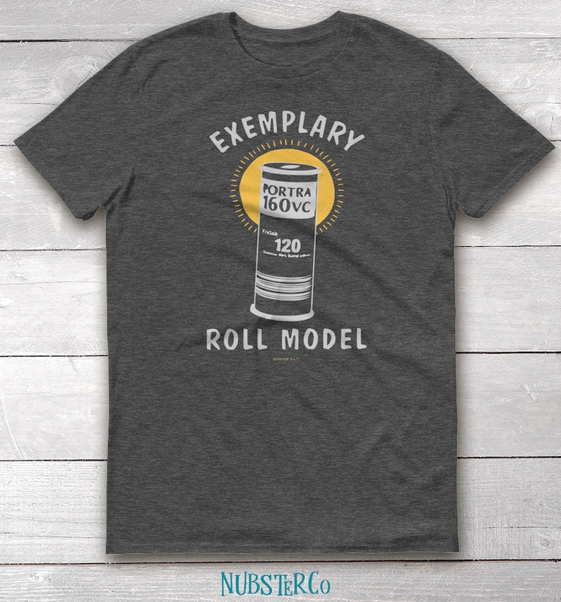 May include: A dark gray t-shirt with the text "EXEMPLARY" above a graphic of a roll of Portra 160VC film and the text "ROLL MODEL" below the graphic.