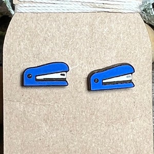 May include: A pair of blue stapler stud earrings. The earrings are made of wood and have a realistic stapler design.