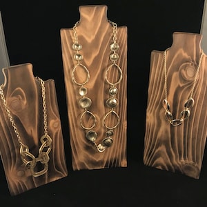 May include: Three wooden necklace displays with gold-toned necklaces. The displays are made of dark brown wood with a natural grain pattern. The necklaces are different styles, including a chain with large links, a chain with small oval links, and a chain with large, flat, round links.
