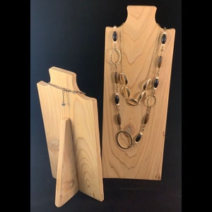 May include: Two wooden jewelry display stands. The larger stand has a gold necklace with black and brown beads on it. The smaller stand has a silver chain on it.