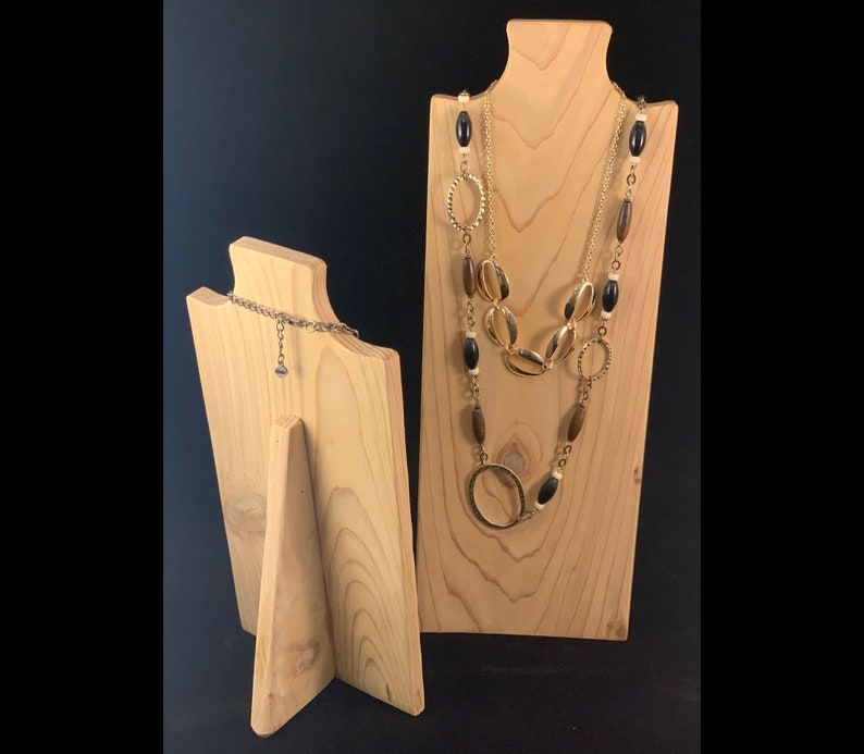 May include: Two wooden jewelry display stands. The larger stand has a gold necklace with black and brown beads on it. The smaller stand has a silver chain on it.