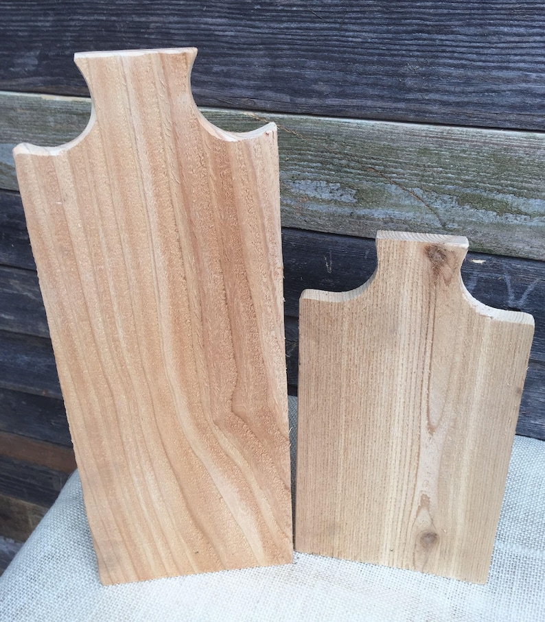 May include: Two wooden cutting boards, one larger than the other, with a natural wood finish. Both boards have a unique shape with rounded edges and a slight curve at the top.