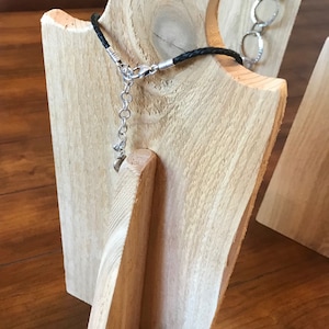May include: A wooden jewelry display stand with a black leather cord necklace. The stand is made of natural wood with a light brown color.