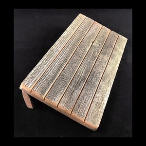 May include: A rustic wooden shelf with a weathered gray finish and a slightly angled design. The shelf is made of multiple planks of wood, creating a natural and organic look.