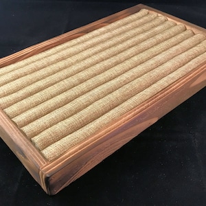 May include: A wooden ring display box with a brown stain. The box has a fabric lining with multiple rows of fabric-covered slots for storing rings.