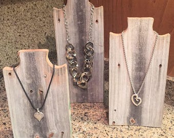 May include: Three rustic wooden necklace displays with different styles of necklaces. The displays are made from reclaimed wood and have a distressed finish. The necklaces are silver and feature heart-shaped pendants.