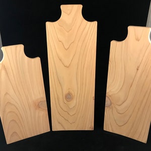 May include: Three wooden cutting boards of varying sizes with rounded edges and a handle on the top. The boards are made of light wood with a natural grain pattern.