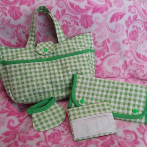 May include: A set of quilted accessories in a green and white gingham pattern. The set includes a tote bag, a wallet, a small pouch, and a wristlet. The bag has a green handle and a green button closure. The accessories are on a pink floral background.