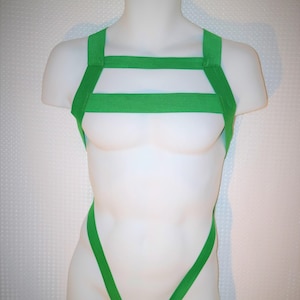 May include: A green body harness with straps that cross over the chest and back. The harness is made of elastic material and has a V-shaped opening in the front.