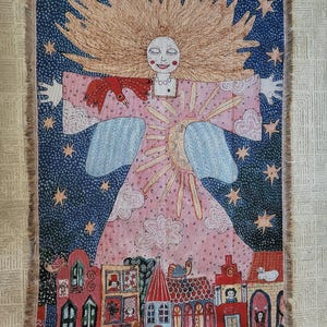 Op de afbeelding: Een geweven wandtapijt met een grillige illustratie. Het toont een figuur met golvend blond haar, een roze jurk en uitgestrekte armen. De achtergrond is een sterrenhemel met een rij kleurrijke huizen aan de onderkant. Het wandtapijt heeft een gefranjerde rand.