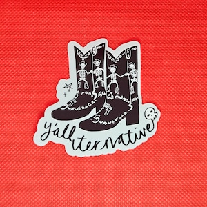 May include: White sticker with a black and white illustration of two cowboy boots with skeletons dancing on them. The text "y'allternative" is written in a handwritten style below the boots.