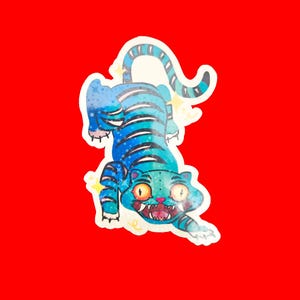 May include: A sticker of a blue tiger with black stripes, stars, and yellow accents. The tiger is crouching with an open mouth and orange eyes. The background is red.