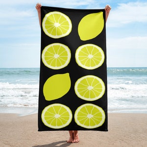 May include: A black beach towel with a repeating pattern of yellow lemons. The lemons are in various shapes and sizes, some are whole and some are sliced.