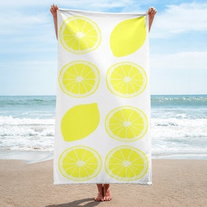May include: A white beach towel with a lemon design. The towel features eight yellow lemons, some whole and some sliced in half.