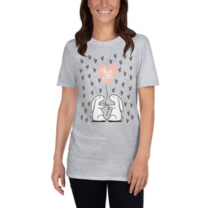 May include: A light gray t-shirt featuring a graphic of two white cartoon bunnies holding hands, with a pink heart-shaped balloon that says "Kiss Love". Small black hearts are scattered around the design.