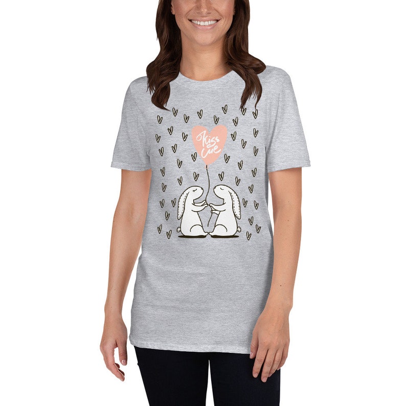 May include: A light gray t-shirt featuring a graphic of two white cartoon bunnies holding hands, with a pink heart-shaped balloon that says "Kiss Love". Small black hearts are scattered around the design.