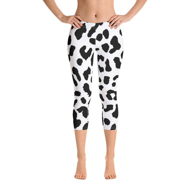May include: Cropped leggings featuring a black and white dalmatian spot pattern. The leggings are mid-calf length and made of a stretchy material. The high-waisted leggings are suitable for various activities, including yoga and running.