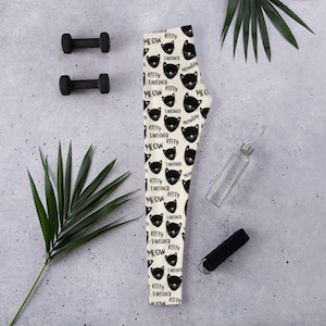 May include: Black and white leggings with a repeating pattern of black cats with the text "Meow Kitty Takeover" on a cream background.