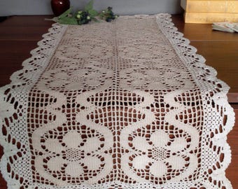 May include: A white crocheted table runner with a floral design. The runner has a scalloped edge and is made of delicate crochet stitches.