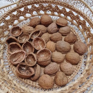 May include: A wicker basket containing whole and cracked walnuts. The walnuts are a light brown colour, and the basket has a natural, woven texture. Some shells are empty.