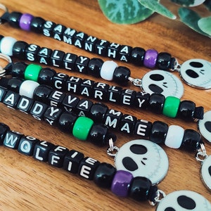 May include: Six black beaded keychains with different names spelled out in white letters. Each keychain has a silver ring and a round charm with a black and white Jack Skellington face.