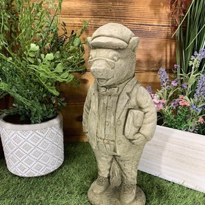 May include: A grey stone garden statue of a bear wearing a hat, glasses, and a suit. The bear is holding a book in its right hand.