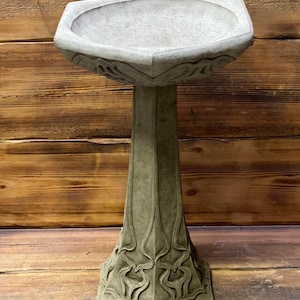 May include: A grey concrete bird bath with an ornate design. The bath is on a pedestal with a hexagonal base.